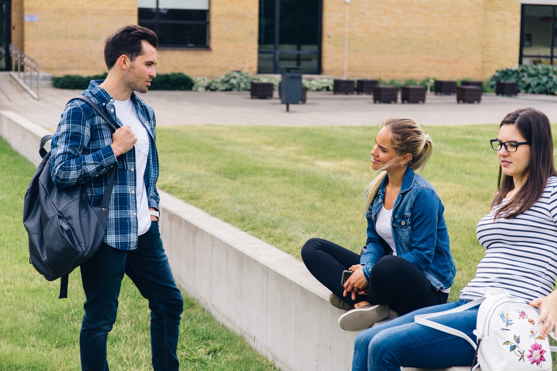 Tre studenter samtalar på en gräsmatta utanför ett tegelhus på campus