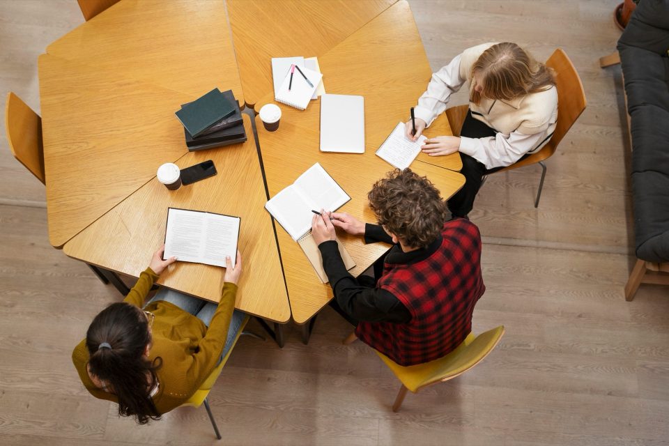 Studiegrupp sedd ovanifrån kring ett runt träbord med böcker och papper