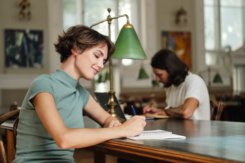 Student antecknar vid ett bord i ett bibliotek med grön läslampa